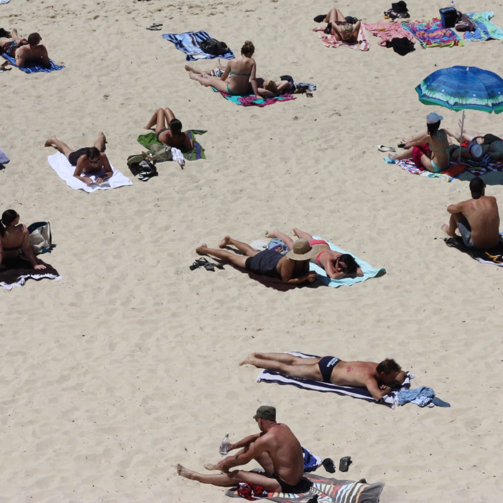personas tomando sol en la playa, exposición solar que aumenta el riesgo de melanoma